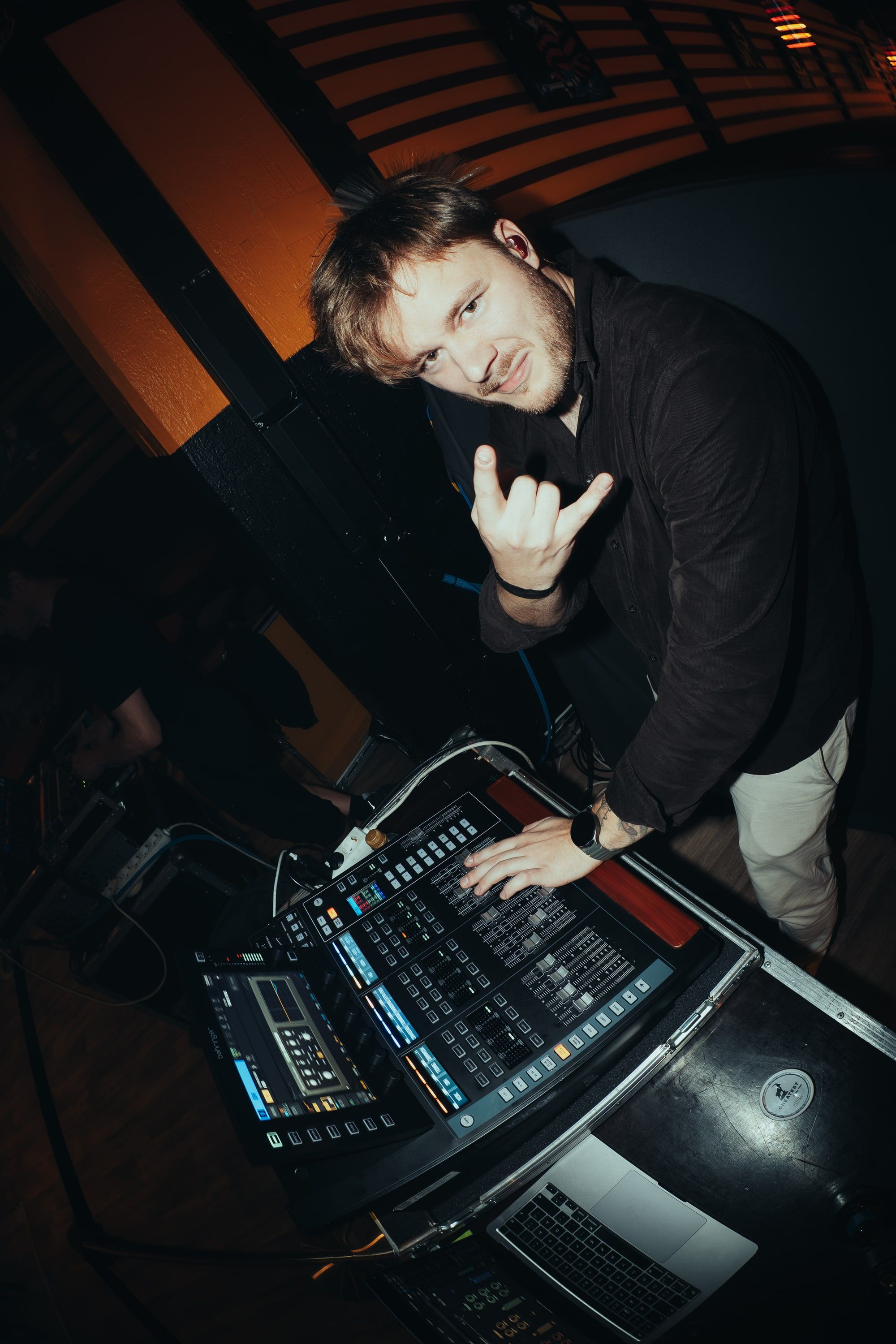 Akseli Kallunki leaning over the mixing desk, looking up at the camera and throwing the horns.