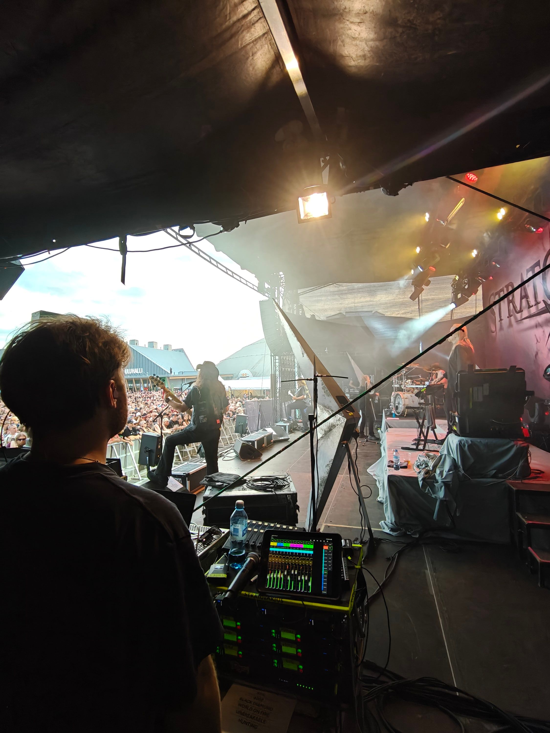 View from the monitor position past Akseli Kallunki onto the festival stage and a large crowd.