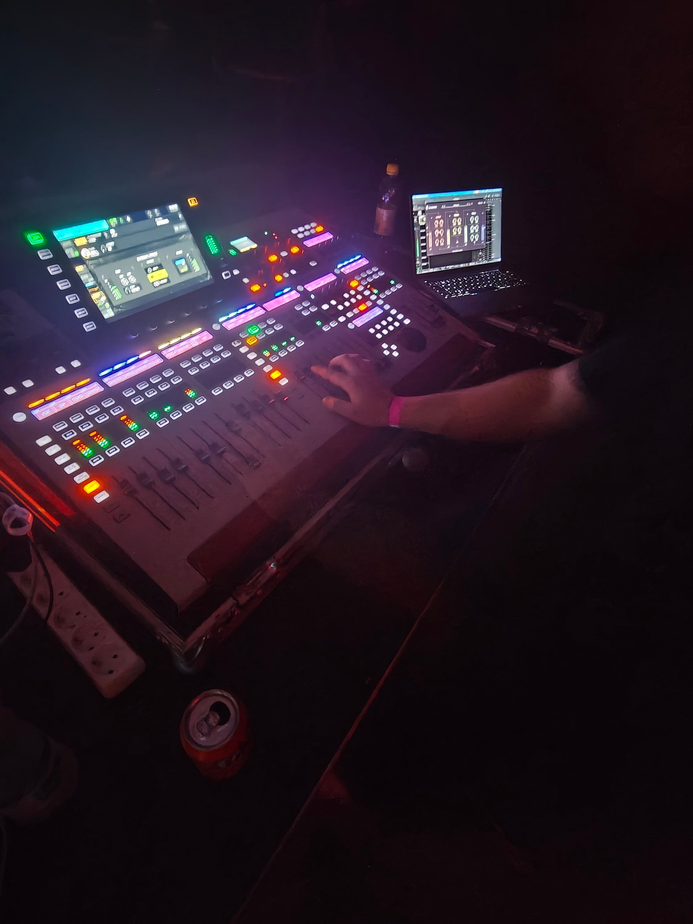 Close-up of a hand on the faders of a lit digital mixing console in a dark room.