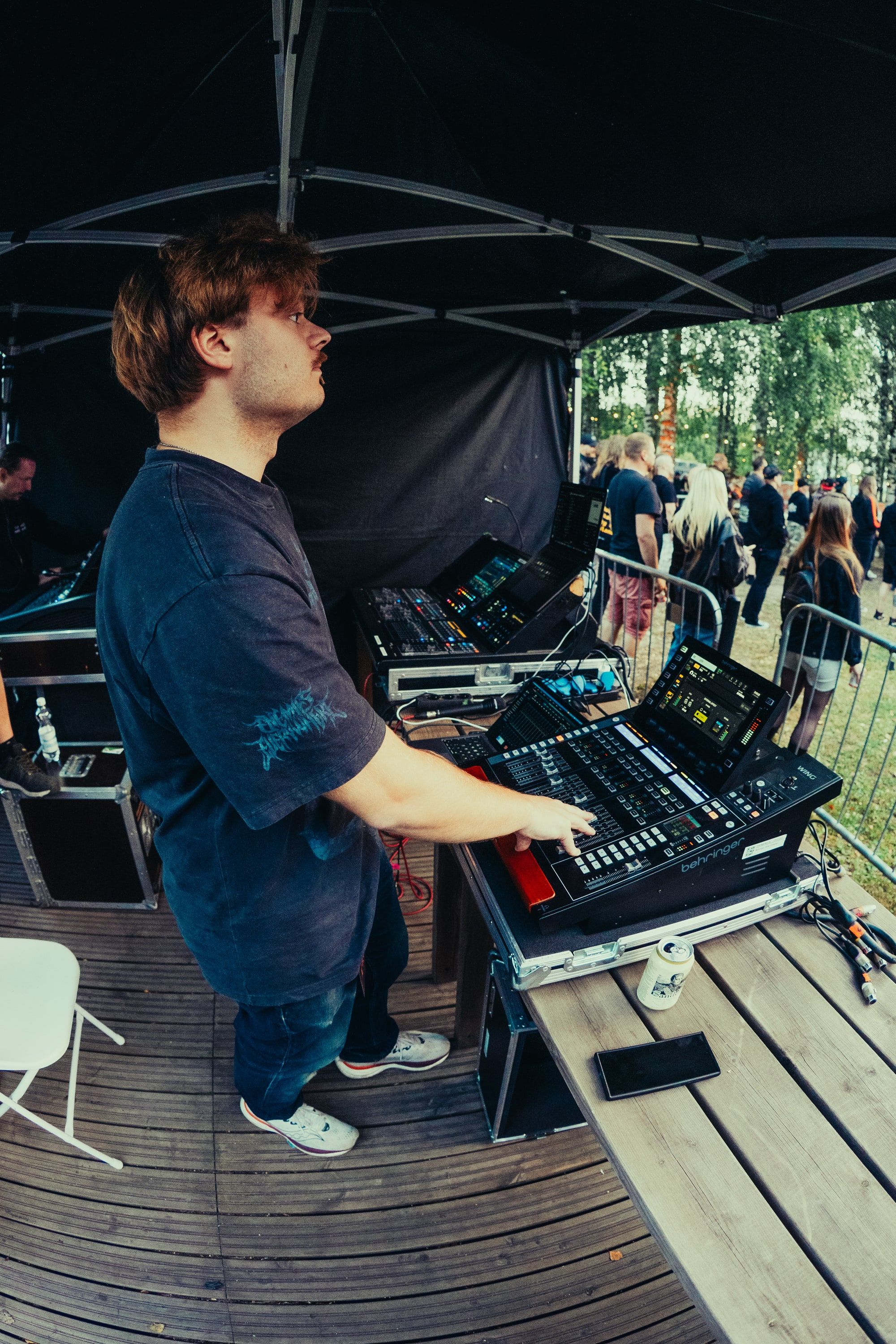 Akseli Kallunki mixing front of house at an outdoor festival, one hand on the faders, the crowd behind the barrier.