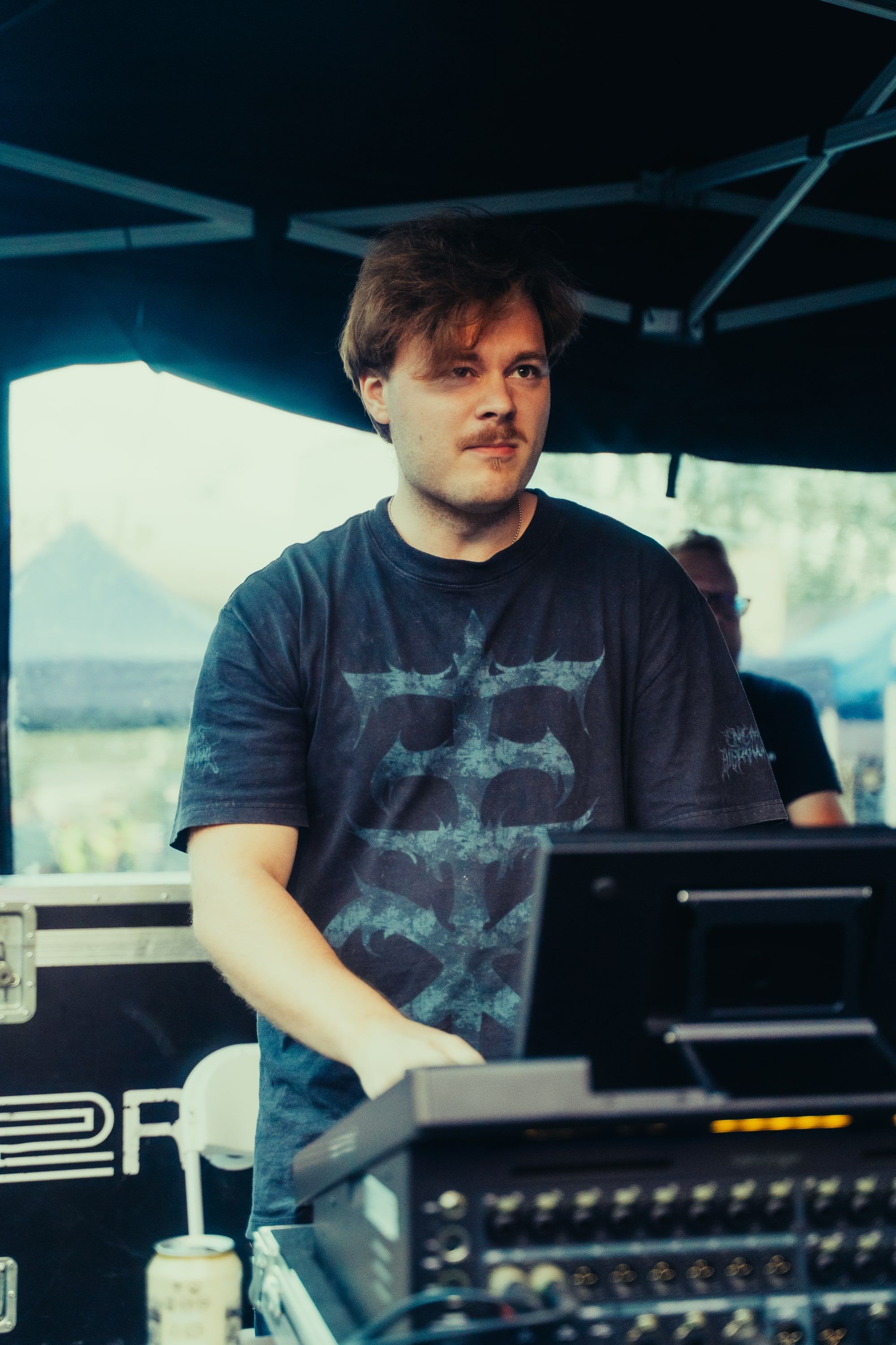 Akseli Kallunki at the front-of-house desk under a festival tent, looking out towards the stage.