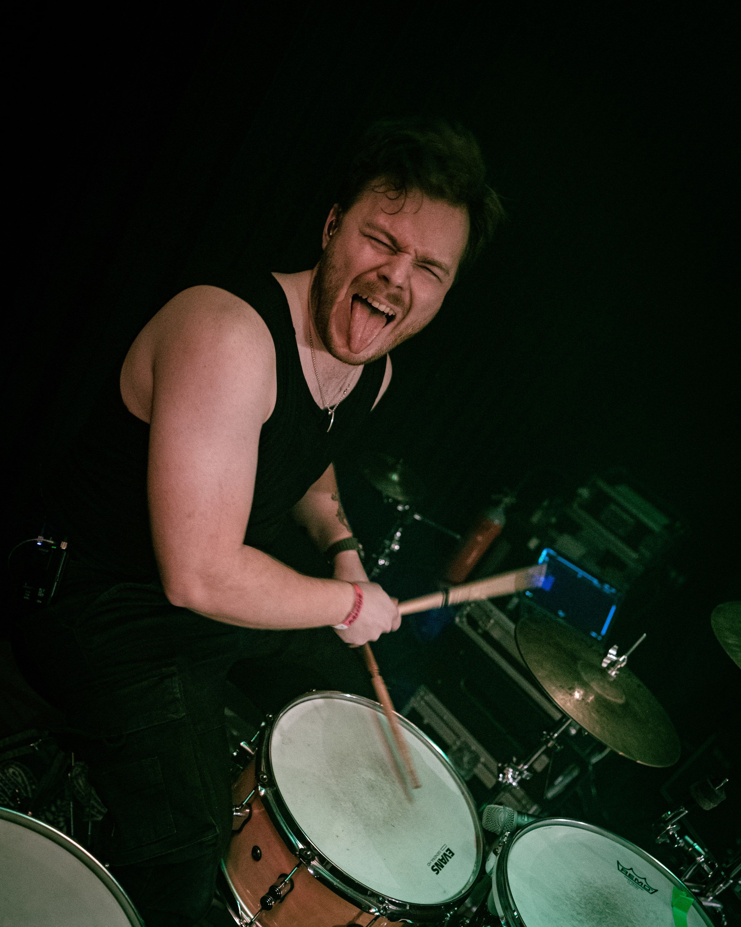 Akseli Kallunki behind the drum kit mid-hit, eyes squeezed shut, tongue out.