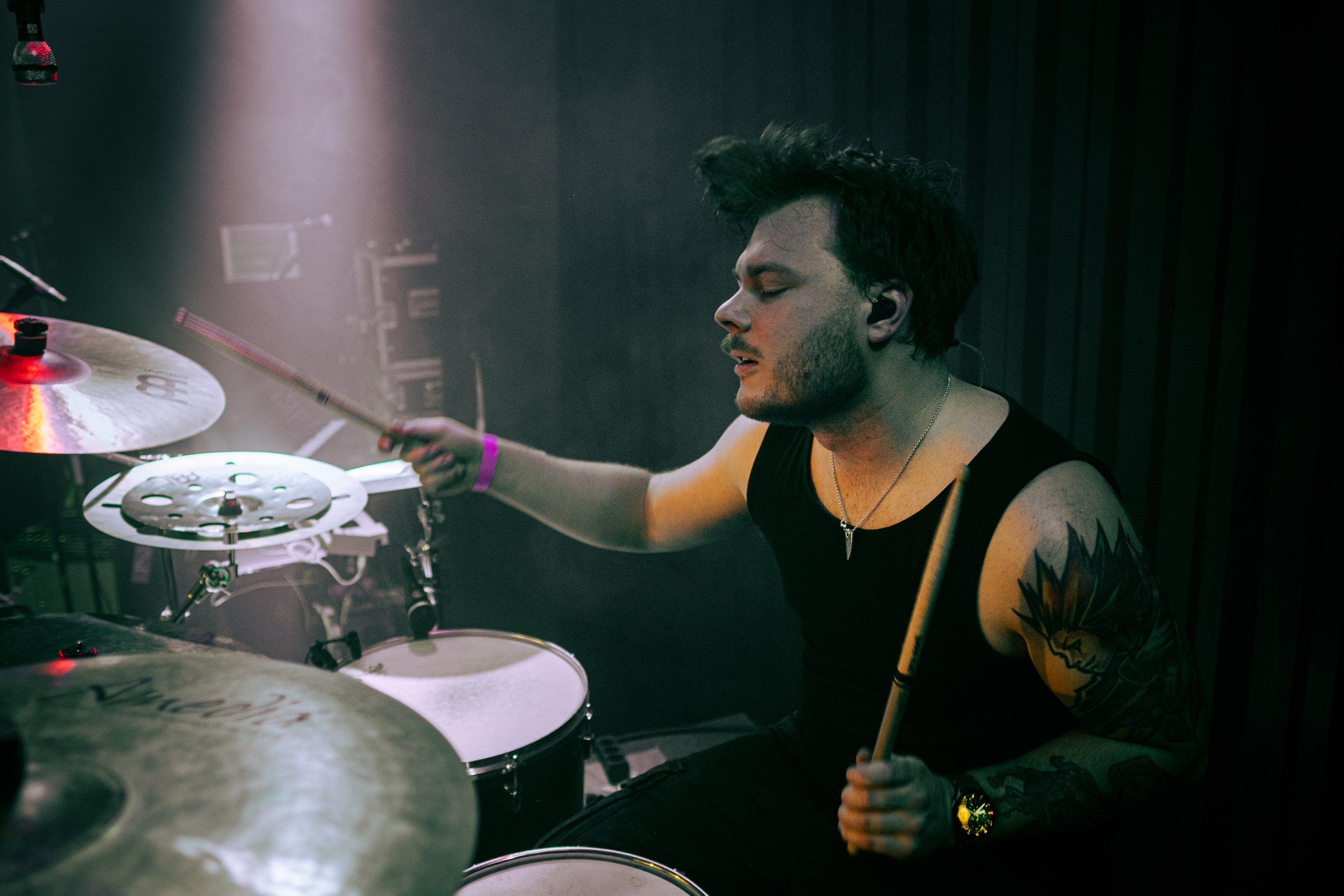 Akseli Kallunki drumming live in a pink stage light, eyes closed, in-ear monitor in.